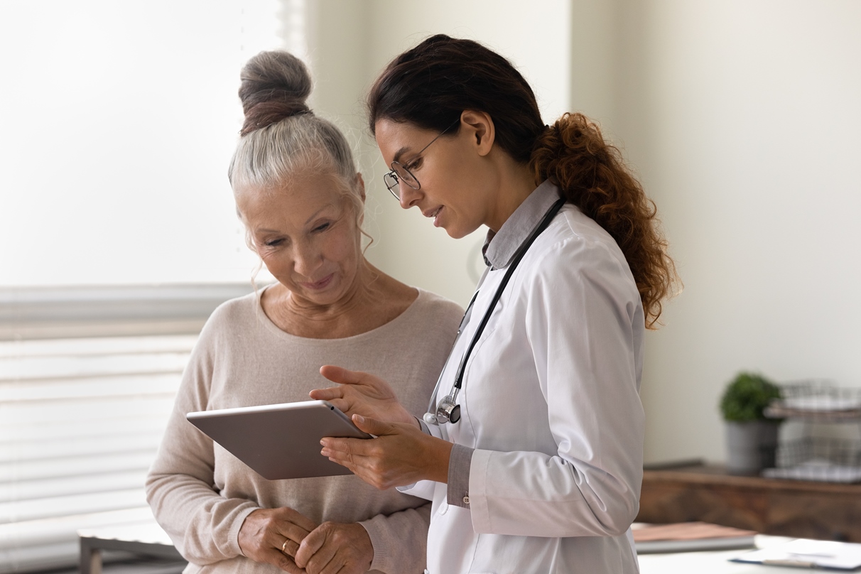 Medical professional showing testing results on tablet screen through the use of clinical LIMS software to older female patient.